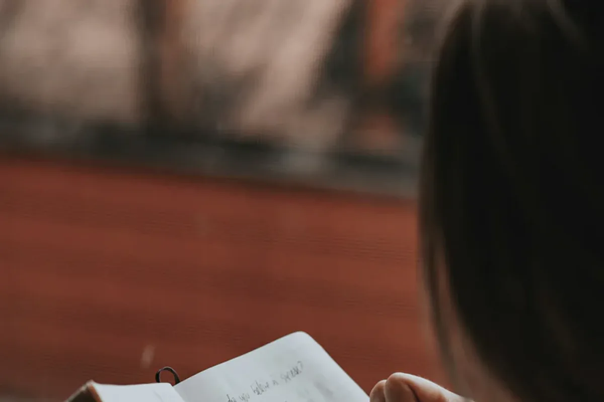 A person sitting by a window at dusk with open hands resting in their lap, quietly letting go.