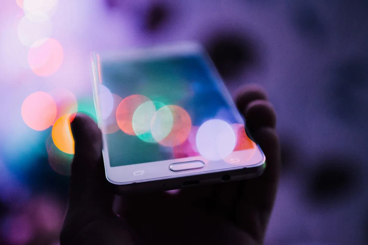 Hand holding a smartphone against soft coloured lights