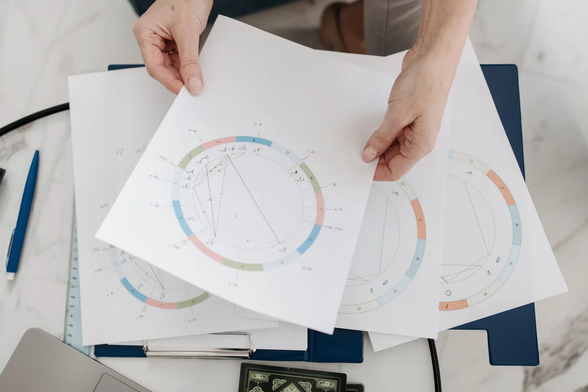 Hands holding printed astrology charts and diagrams