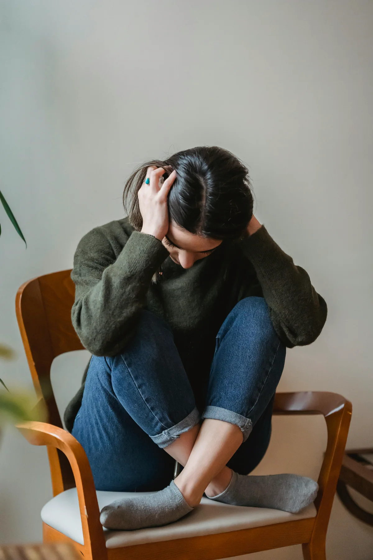 A woman sits curled up on a chair with her hands on her head
