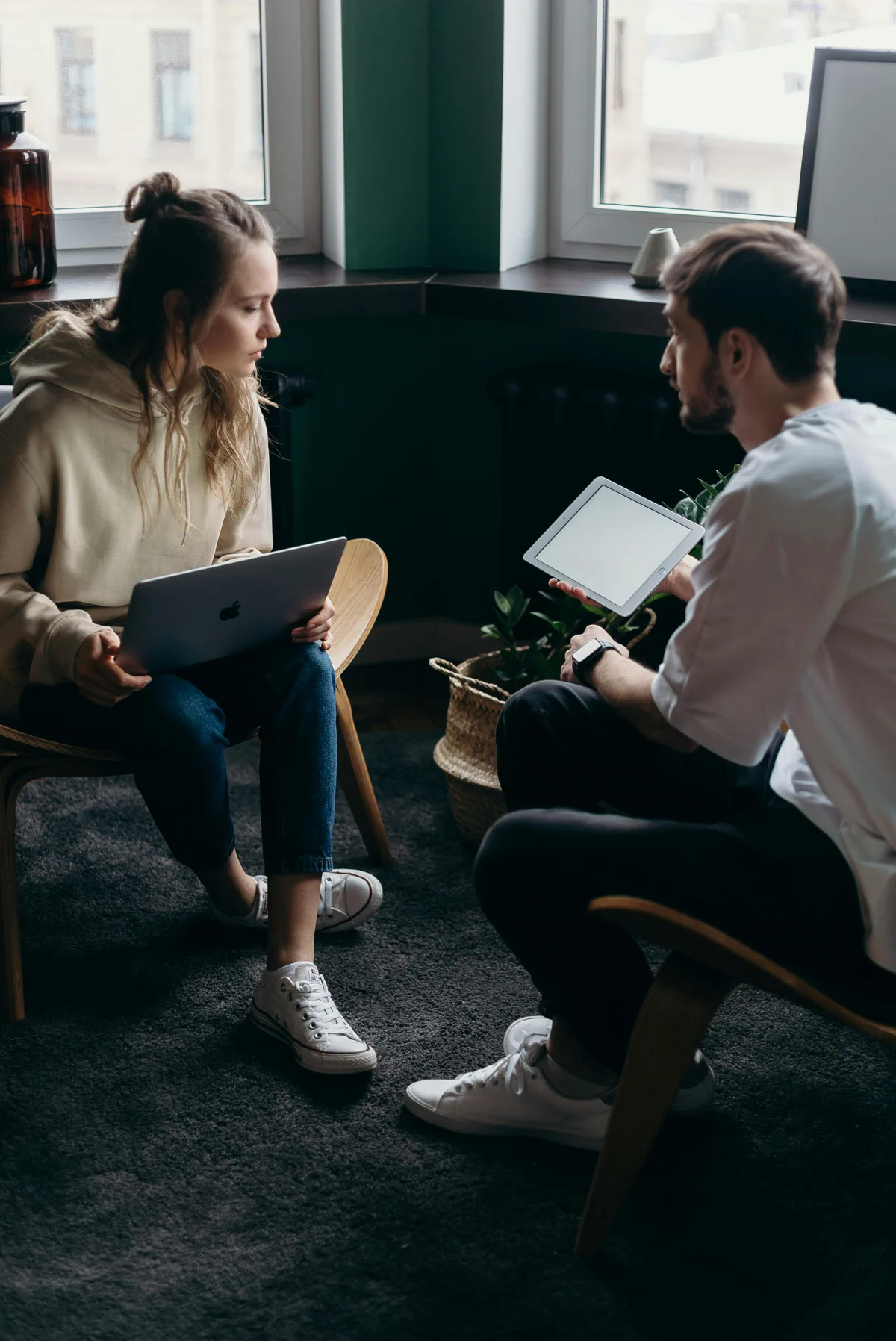 Two people sit facing each other with laptops and a tablet