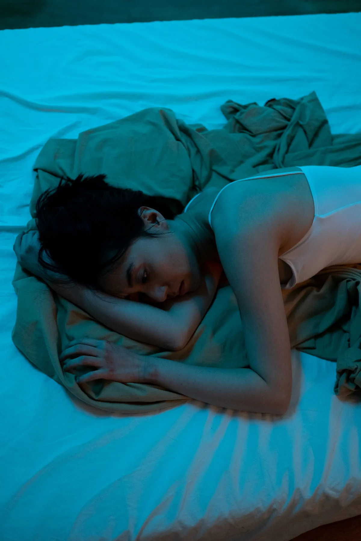 A woman lies awake in bed under blue light
