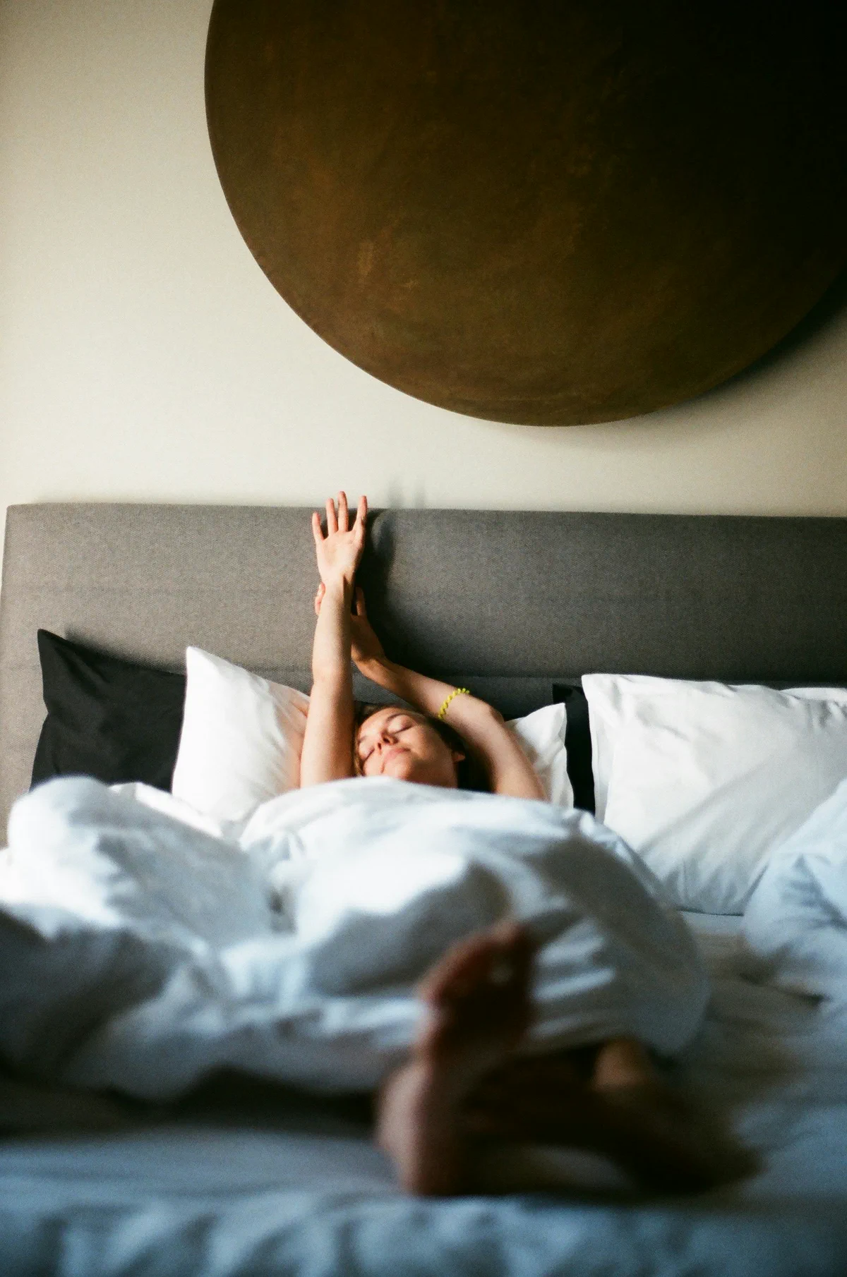 A woman stretches her arms while waking in bed