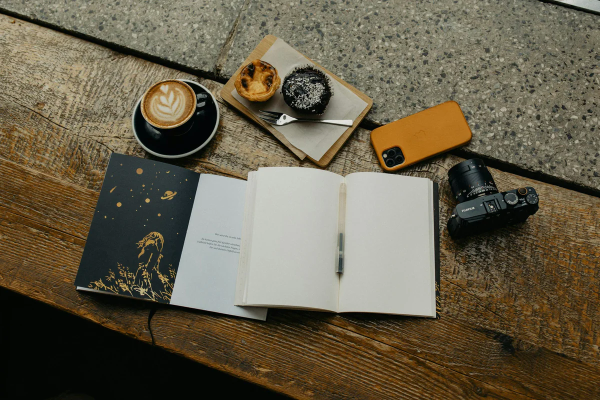 Open journal beside a phone, camera and coffee