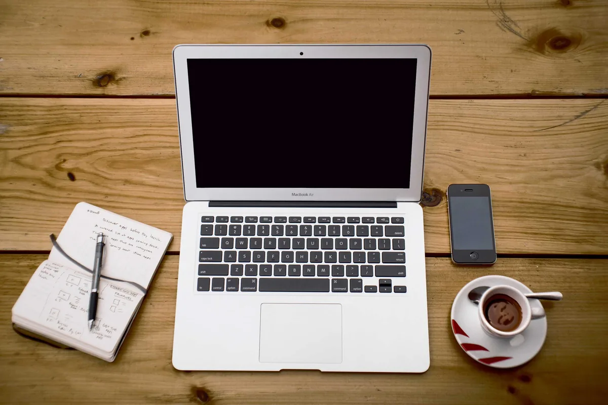 An organized desk with a laptop, notebook and coffee, seen from above