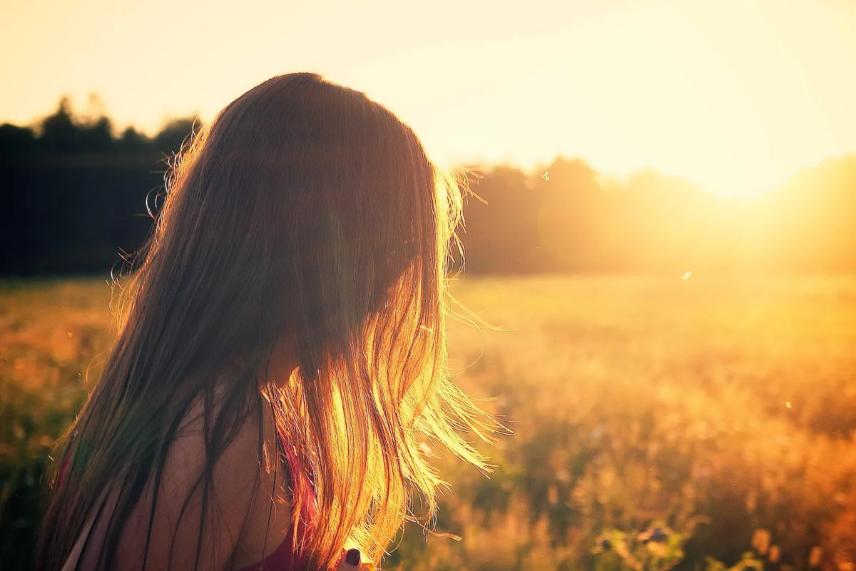 A young woman standing in a sunlit field at golden hour