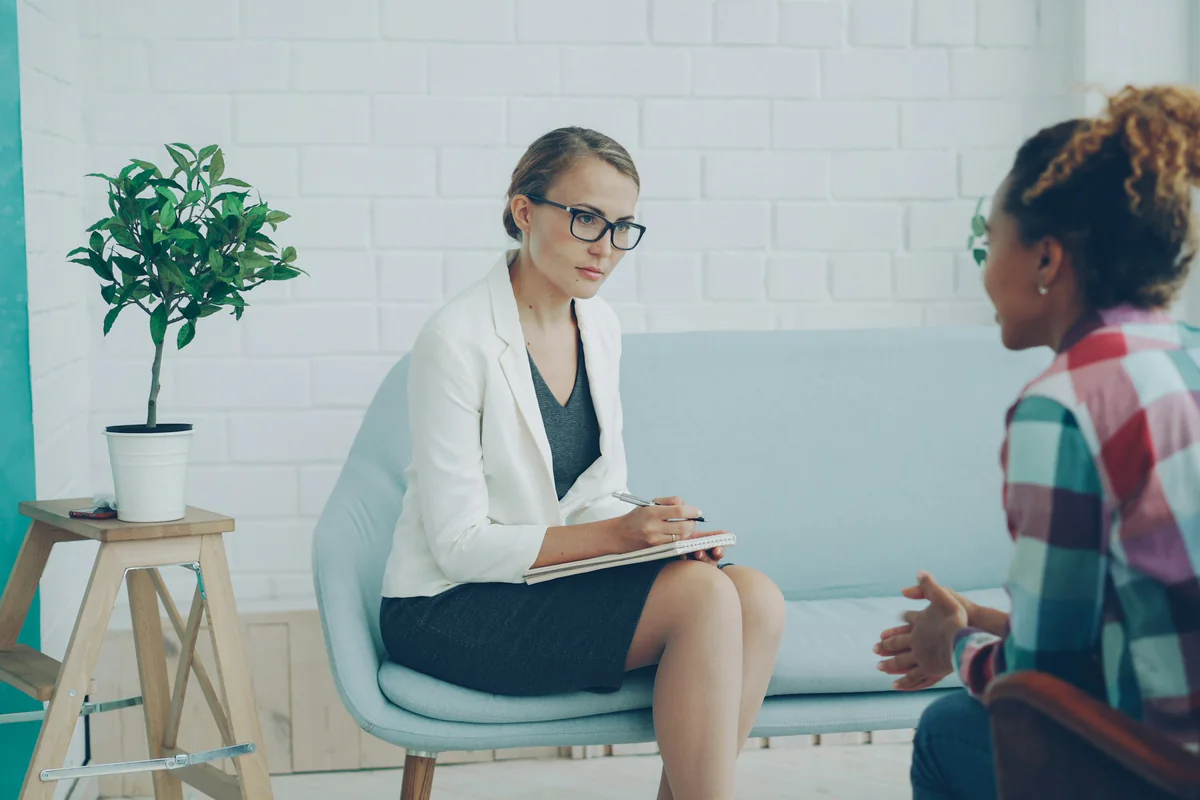 Two women talking while one takes notes in a bright room
