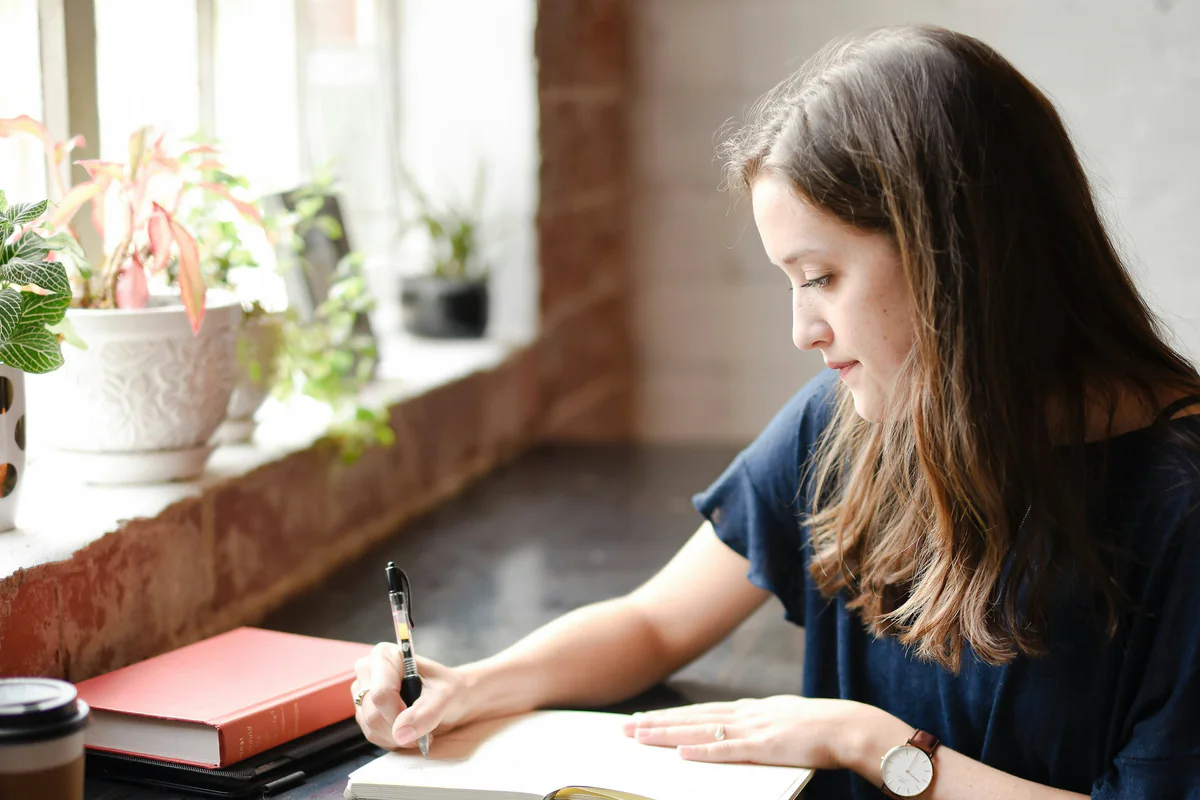 Woman writing in a journal beside a sunlit window