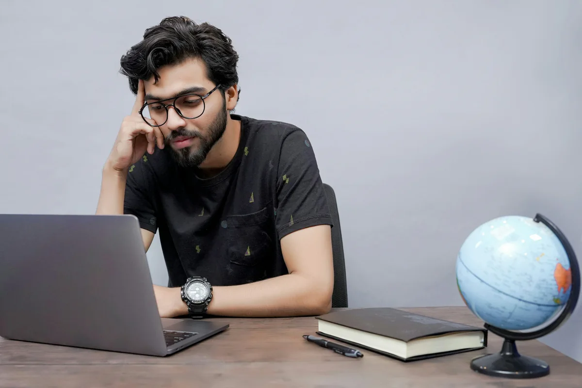 A person using a laptop beside books and a globe